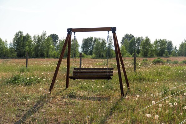 A wooden swing set in a grassy field with trees in the background.