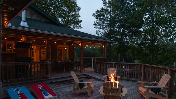 A wooden deck with Adirondack chairs, a fire pit, and a deck with string lights. - Tranquil Oasis in Trent Lakes w/ Private Ponds, Fire Pit, Game Room & Hot Tub (Bobcaygeon)