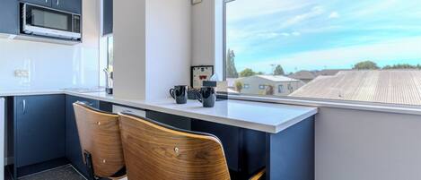 Una cocina moderna con armarios oscuros, un microondas y una ventana que ofrece vistas a edificios. Dos sillas de madera están ubicadas en la barra.