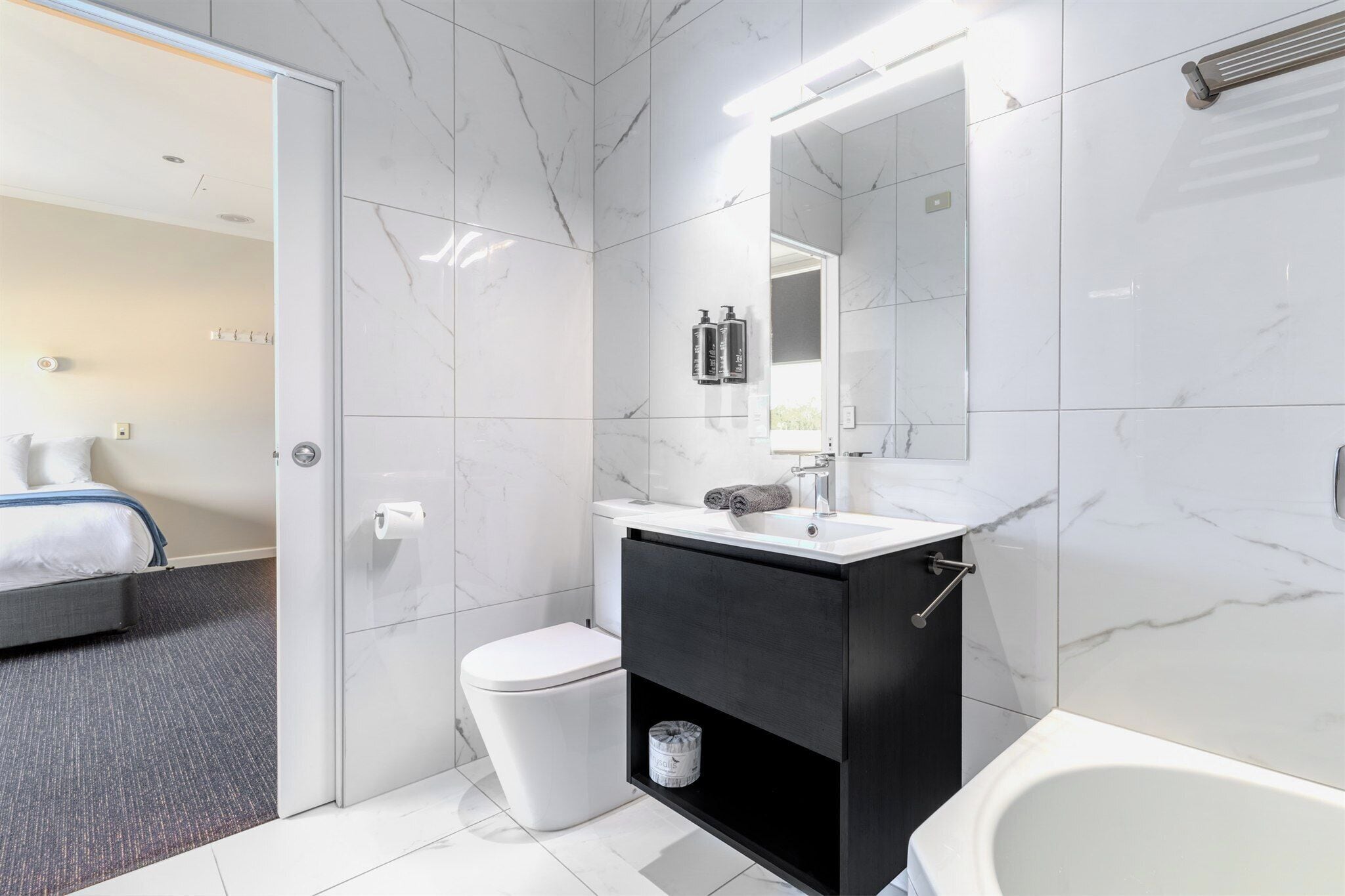 Et moderne badeværelse med toilet, sort kommode, spejl og badekar.