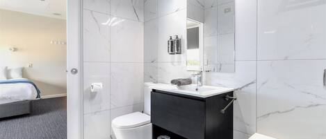 Et moderne badeværelse med toilet, sort kommode, spejl og badekar.