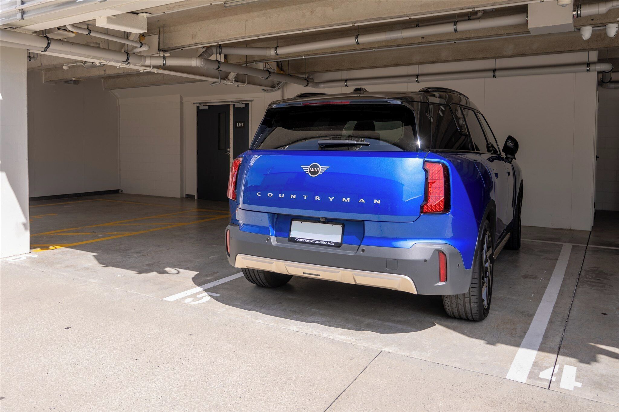 A blue SUV parked in a parking garage with a lift door in the background.
