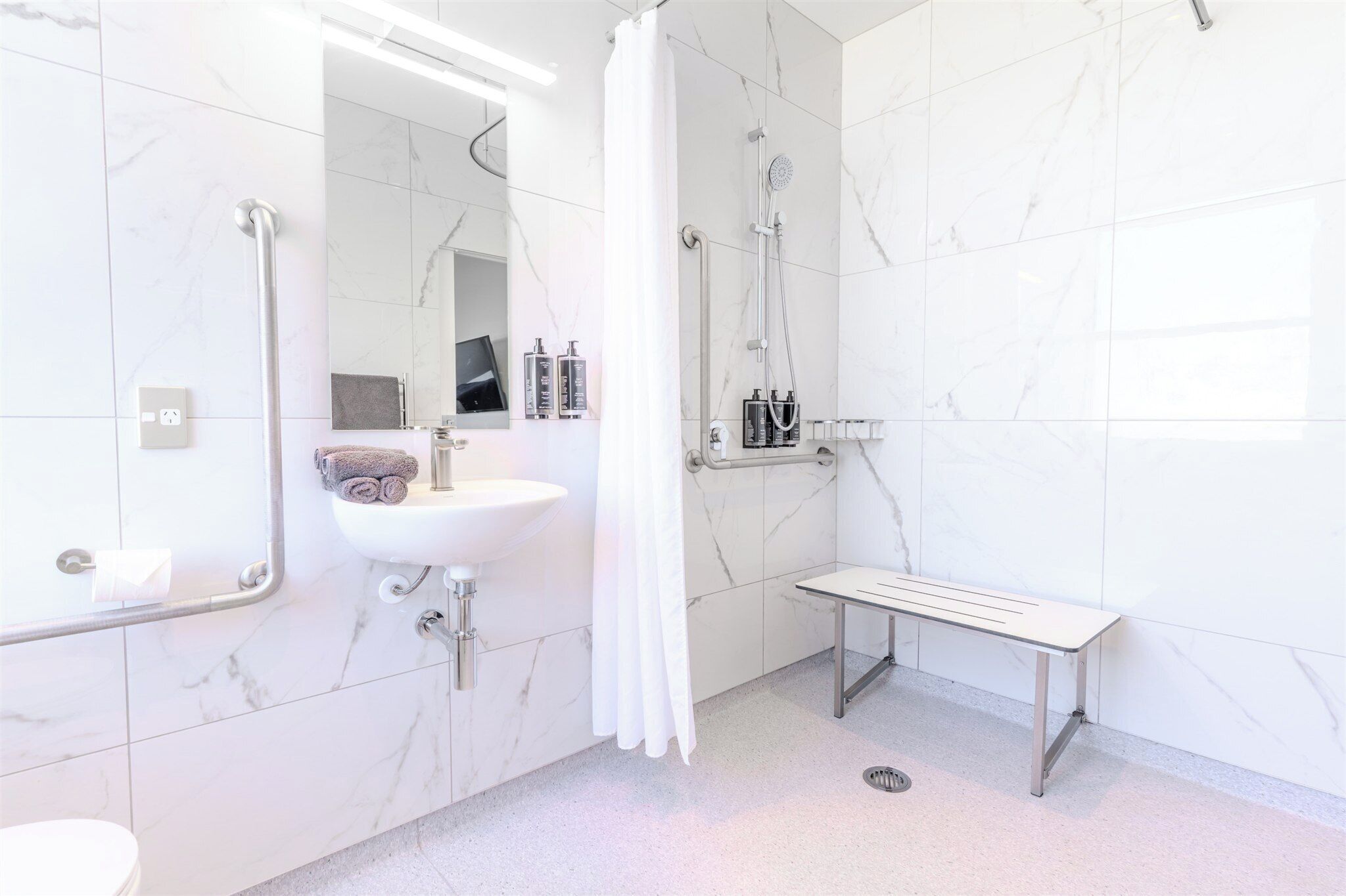 Ein modernes Badezimmer mit Waschbecken, Spiegel, Dusche und Ablagebank.