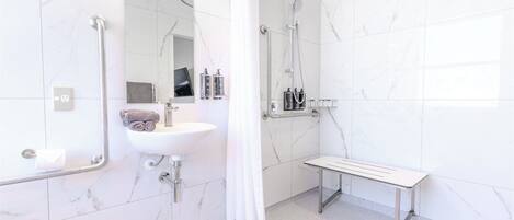 Un baño moderno con lavamanos blanco, espejo, ducha y banco.