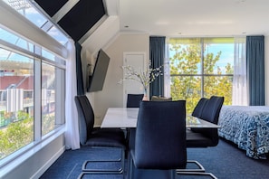 A hotel room with a large window, a bed, a desk with two chairs, and a TV mounted on the wall. - Hamilton Motel 2025 Limited (Hamilton)