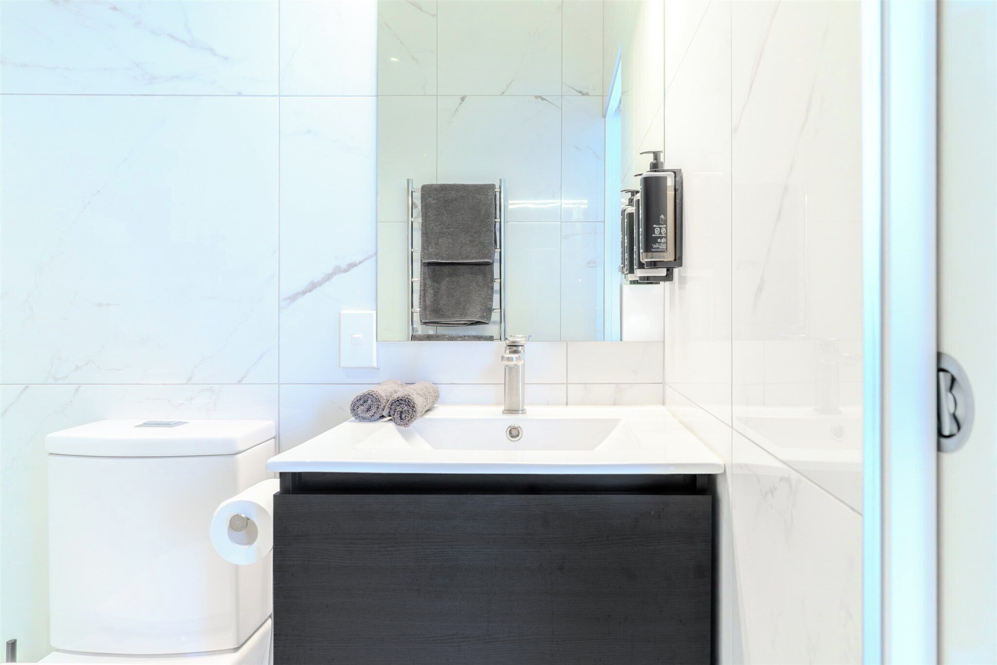 Un baño moderno con un lavamanos blanco, un espejo y un perchero para toallas.
