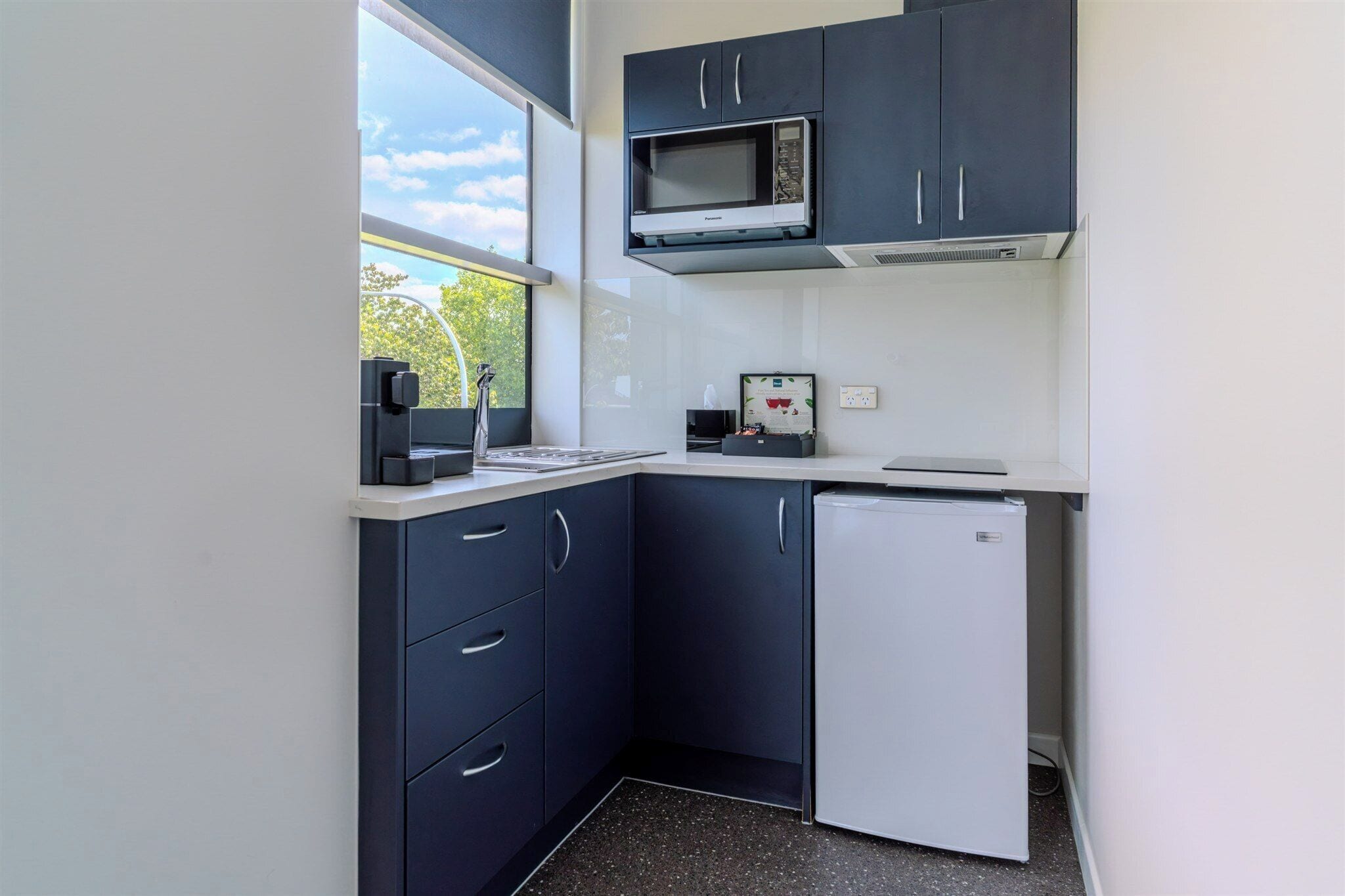 A compact kitchen with dark cabinets, a microwave, a refrigerator, and a window providing natural light.