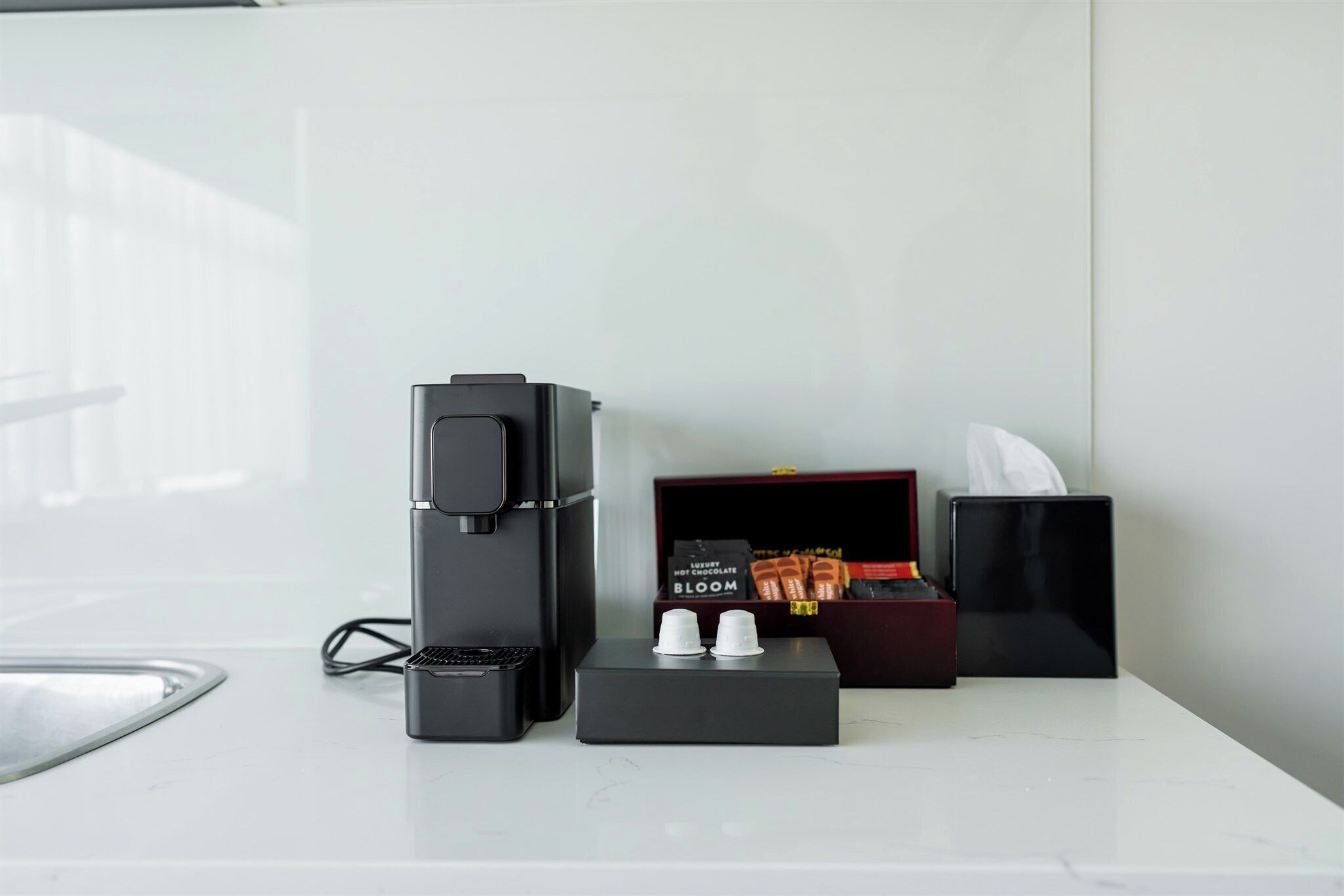 A modern coffee machine, a box of luxury chocolate, and a tissue box on a white countertop.
