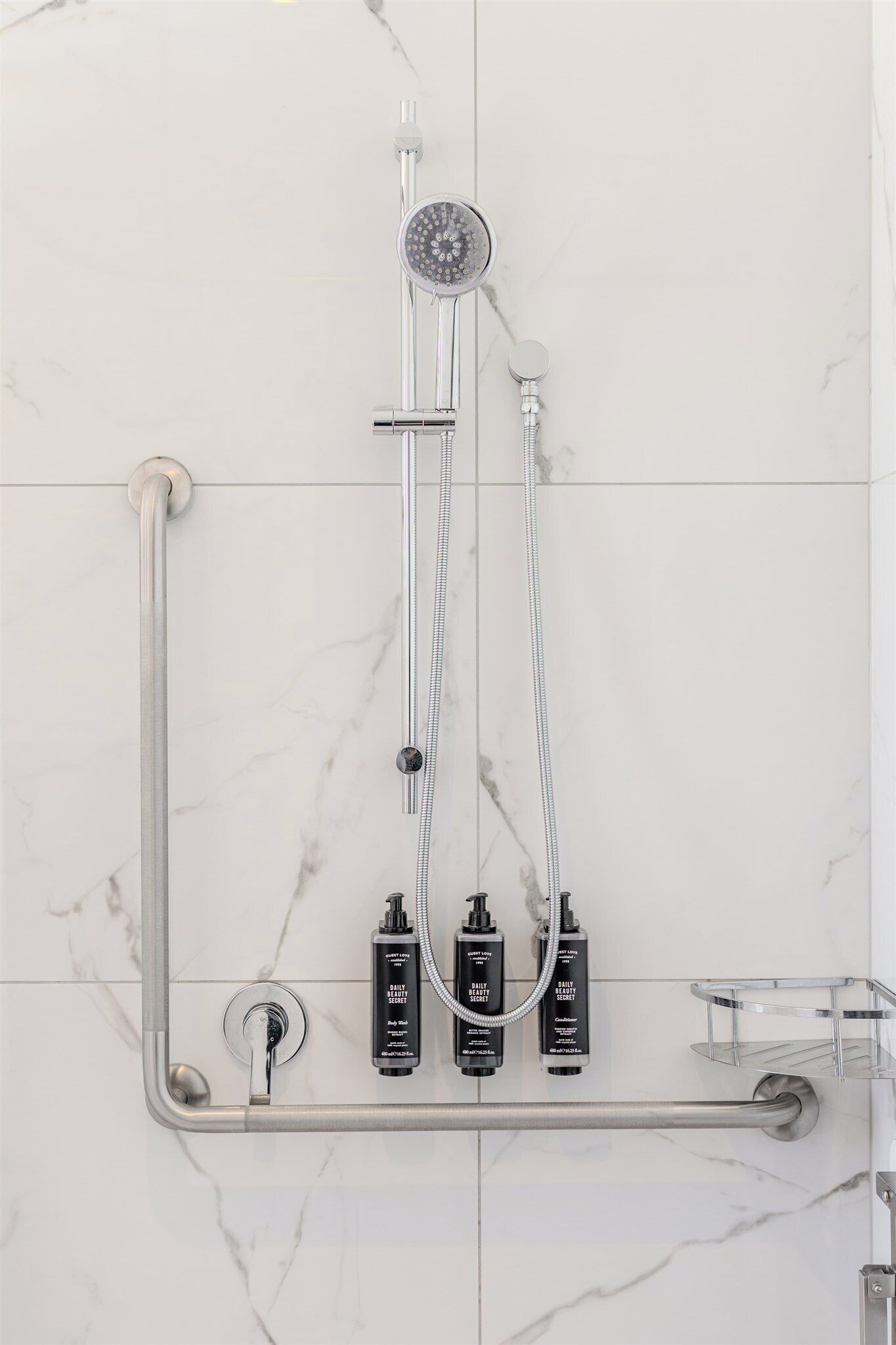 Un baño con ducha, barras de apoyo y dos botellas de champú.