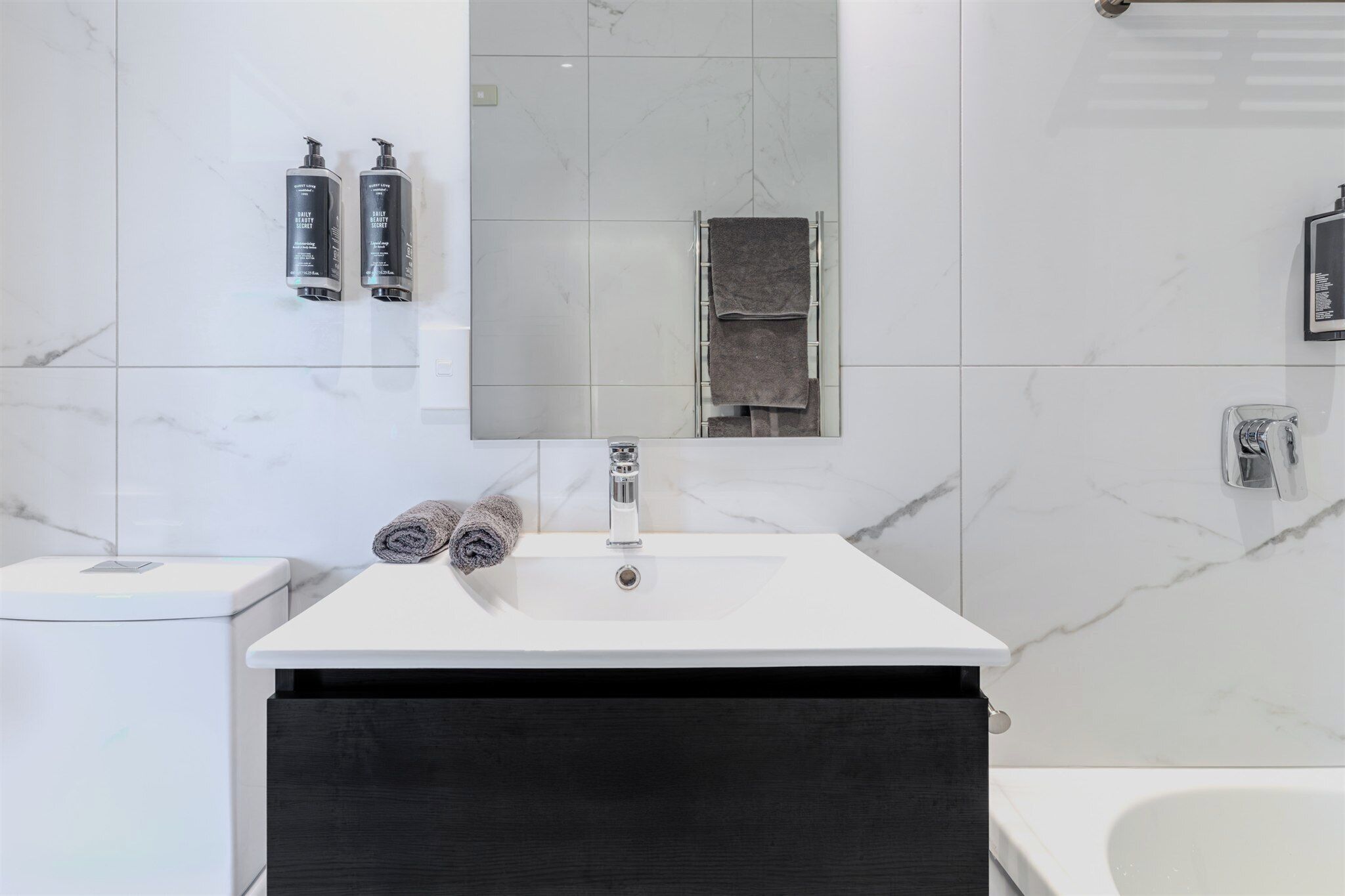Ein modernes Badezimmer mit einem weißen Waschbecken, einem Spiegel und zwei Shampooflaschen.