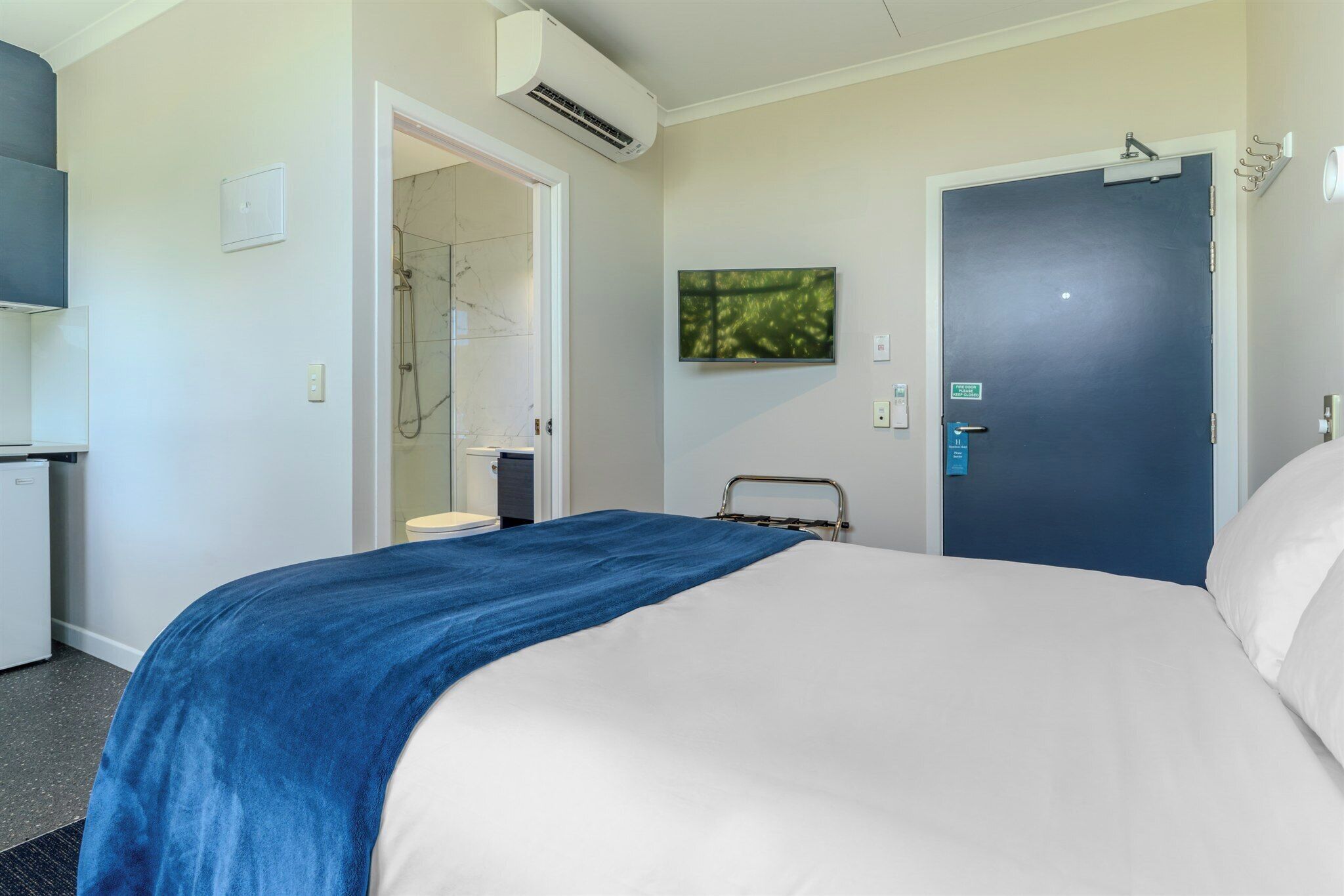 Une chambre d’hôtel avec un lit, une douche, une télévision et une porte avec une pancarte.