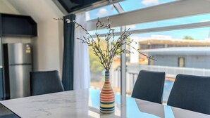 Un espace de repas moderne, avec une table en marbre, un vase rayé aux couleurs vives orné de branches, et une vue sur la ville grâce à de grandes fenêtres.