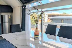 A modern dining area with a marble table, a colorful striped vase with branches, and a view of the city through large windows. - Hamilton Motel 2025 Limited (Hamilton)