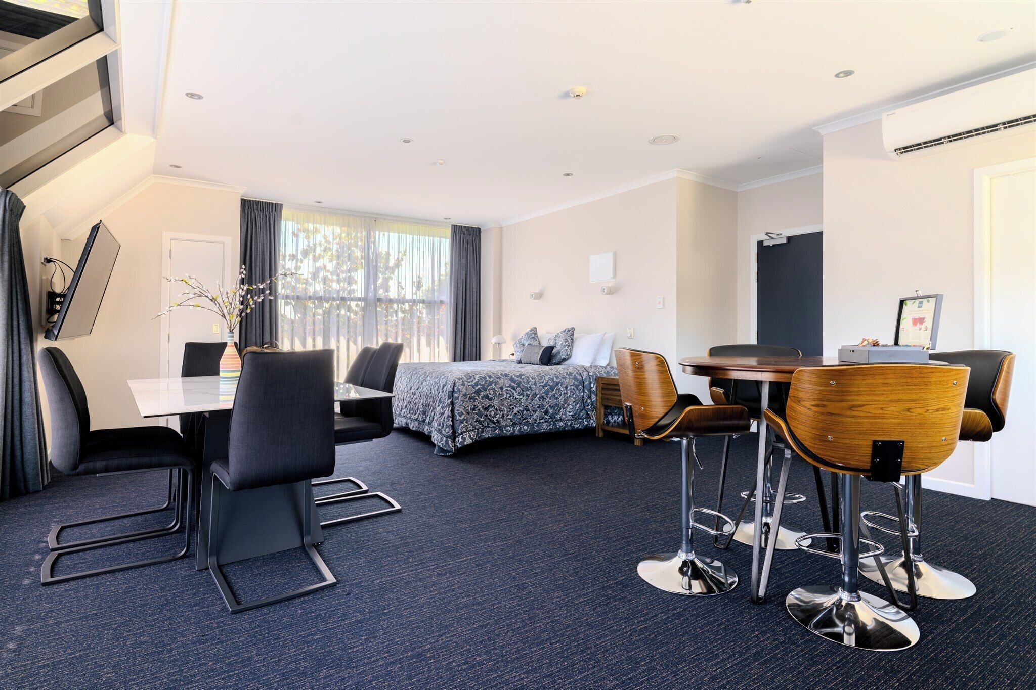 Habitación de hotel con cama, escritorio y sillas, mesa de comedor y una escalera.