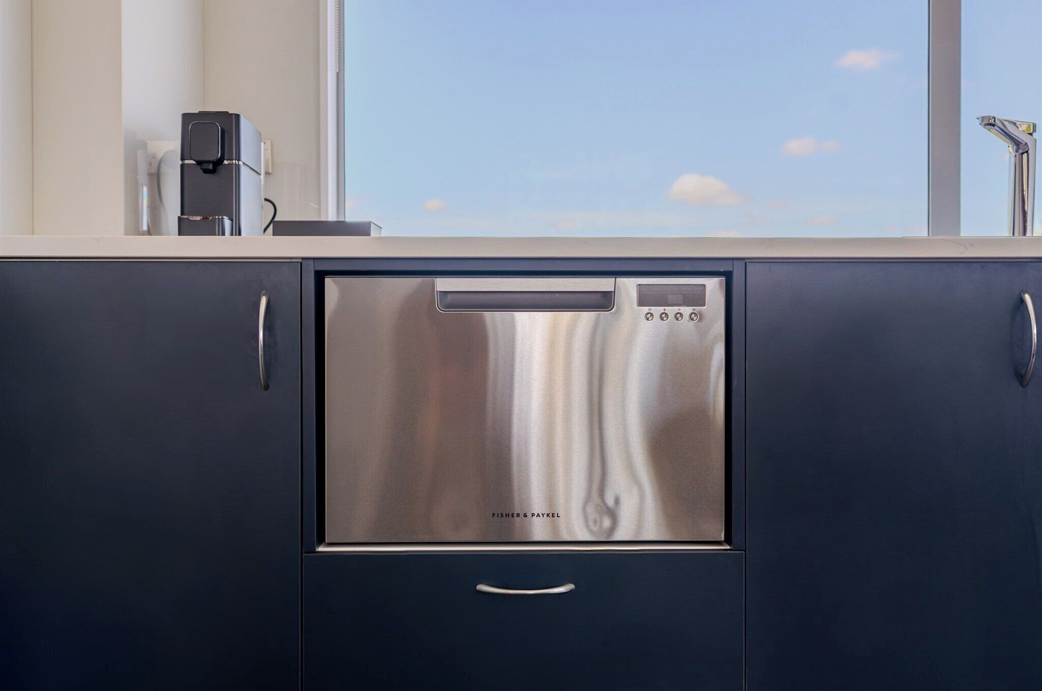 Eine moderne Küche mit Geschirrspüler, Kaffeemaschine und einem Fenster mit Blick zum Himmel.