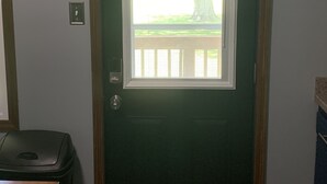 A green door with a window, a light switch, and a doorbell on the wall.