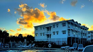 A hotel with a swimming pool, lounge chairs, and a view of the sunset. - No Cleaning Fee! Brand New Double Queen Studio Condo w/ Waterfront Pool + Beach (Southport)