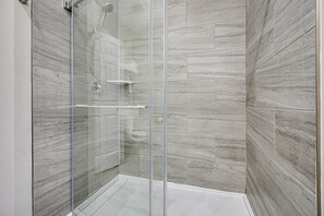 A glass-enclosed shower with a modern design, featuring a marble-like wall texture and a clear glass door.