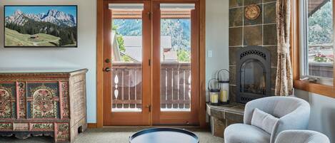 A room with a wooden door leading to a balcony, a fireplace, a decorative cabinet, and a round table.