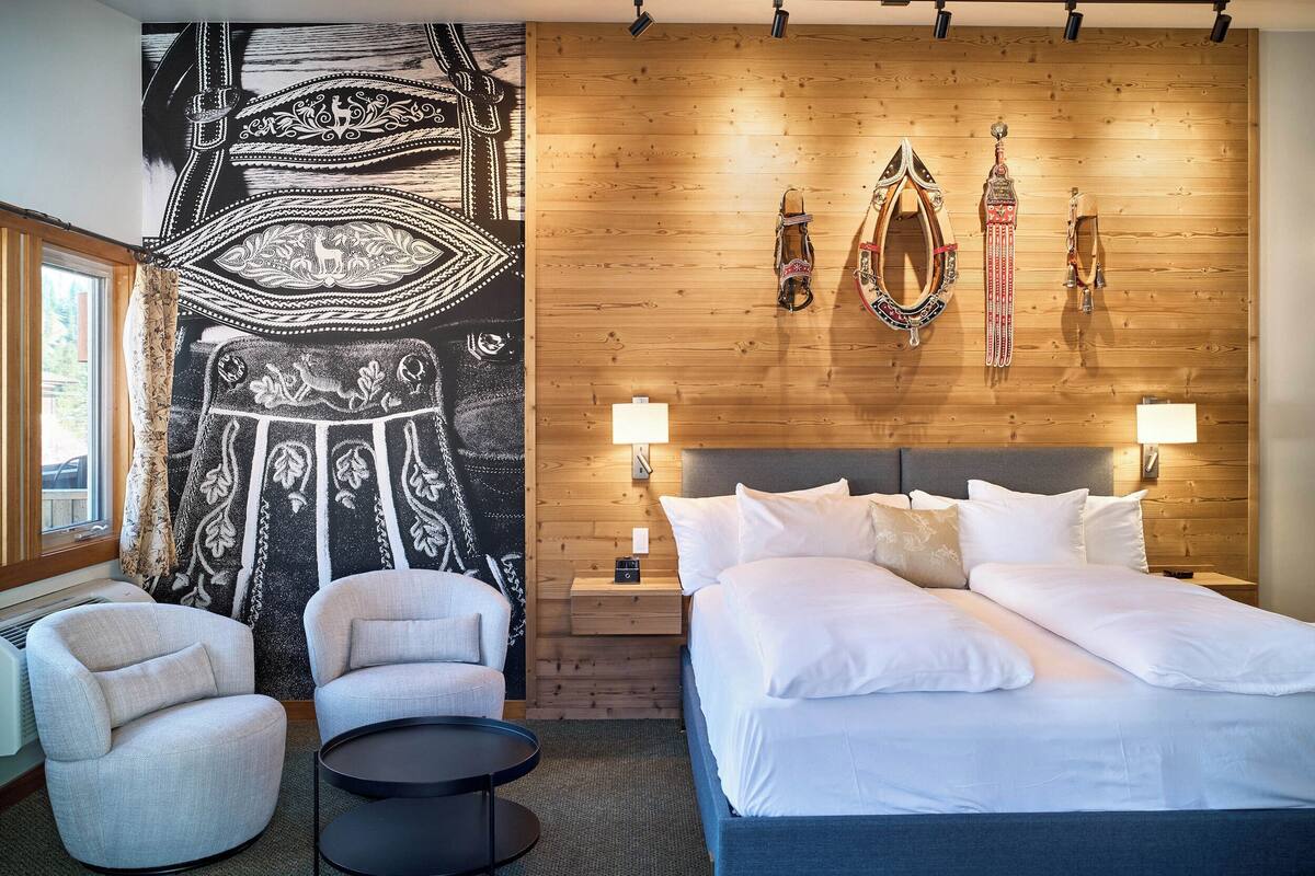 Une chambre d’hôtel avec un grand lit, deux tables de chevet, une petite table, une chaise, une table ronde et un mur décoré.