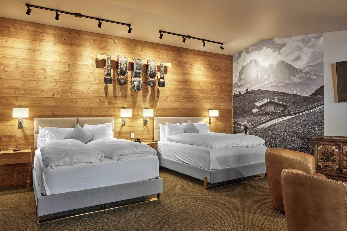Une chambre d’hôtel avec deux lits, des murs recouverts de lambris en bois et une grande fresque représentant un paysage de montagne.