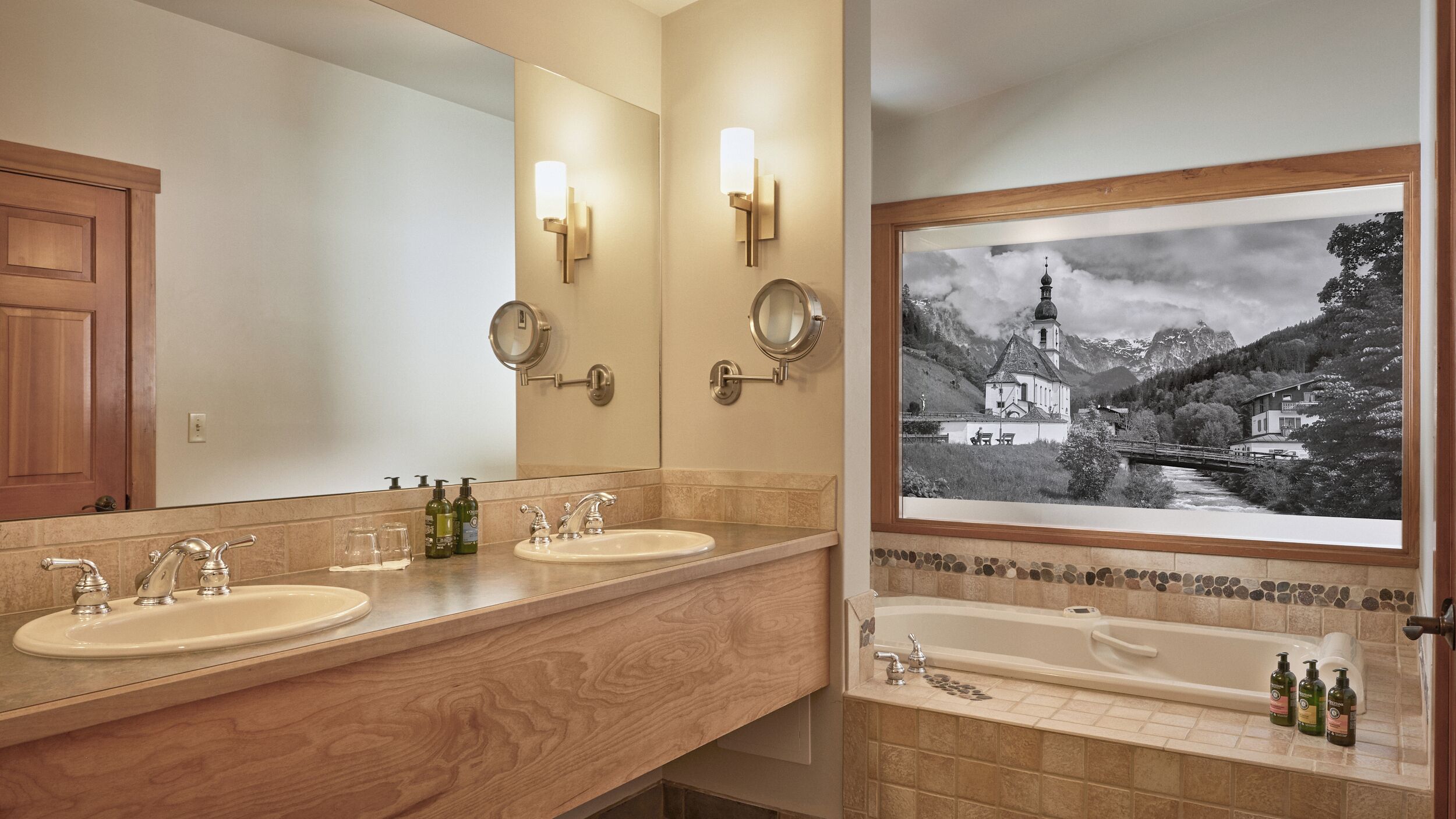 A bathroom with two sinks, a mirror, and a framed black and white photo of a mountain landscape.