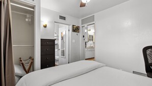 A bedroom with a bed, a dresser, a chair, and a door leading to a bathroom. - Sunlit Palm Cottage in Uptown Phoenix (Phoenix)