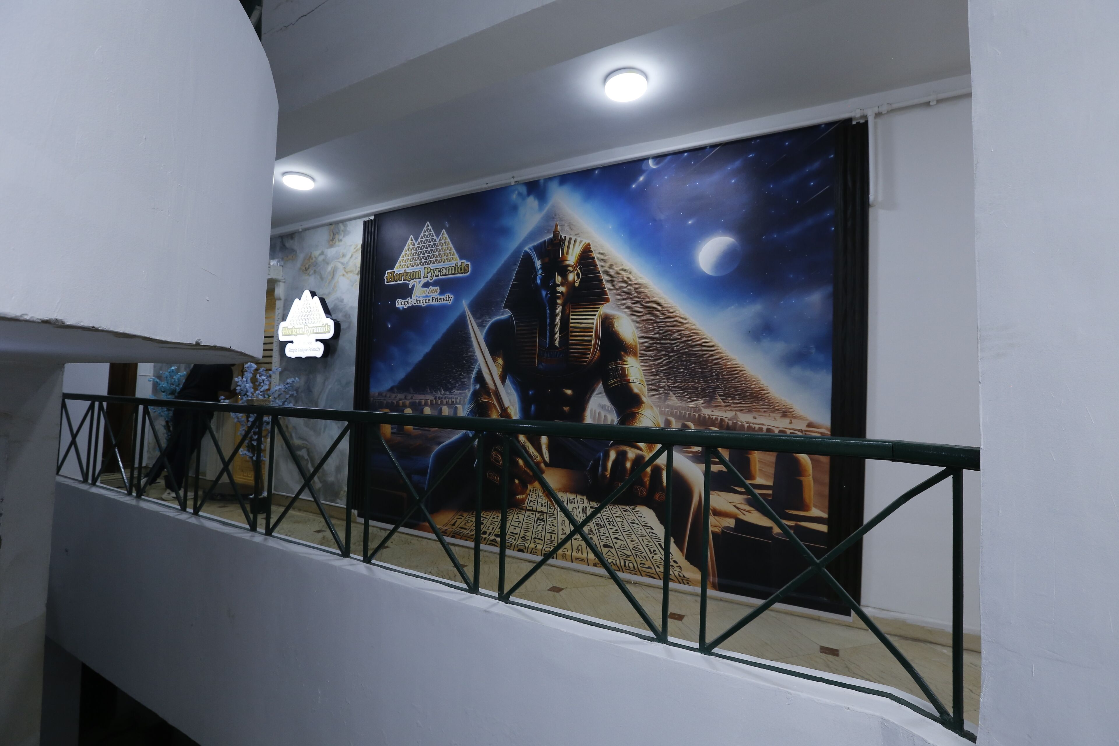 Un pasillo con un mural de la Esfinge y pirámides, un letrero que dice 'Pirámide Egipcia' y una barandilla.