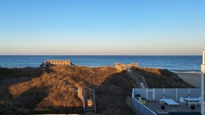Une propriété située en bord de mer, dotée d’une terrasse en bois et de chaises longues offrant une vue sur l’océan.