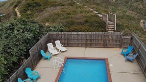 Une piscine rectangulaire dotée d’une terrasse en bois et de chaises longues, entourée d’une clôture en bois, et offrant une vue sur l’océan et la plage en arrière-plan.