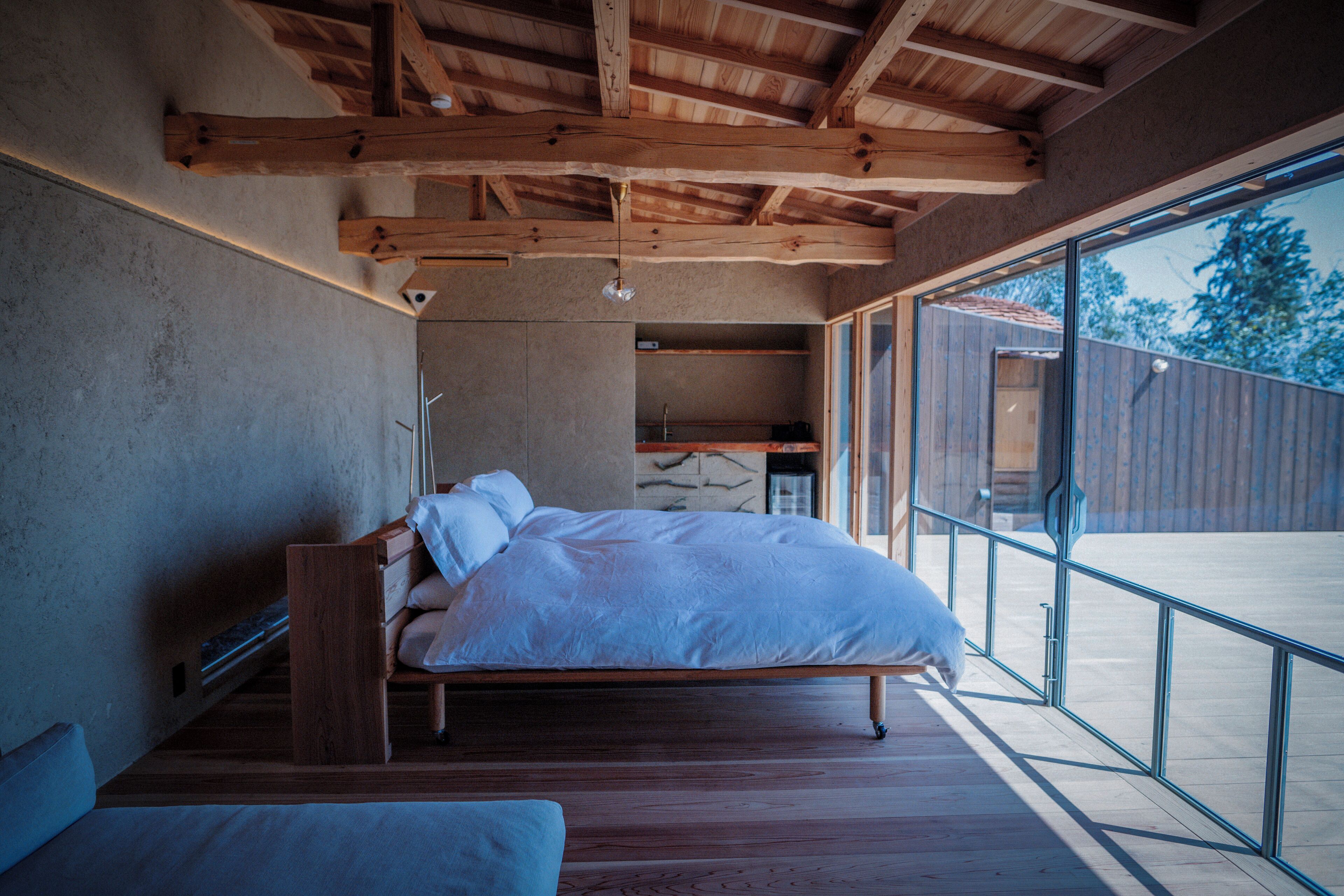 A bedroom with a wooden bed, a bench, and a large window.