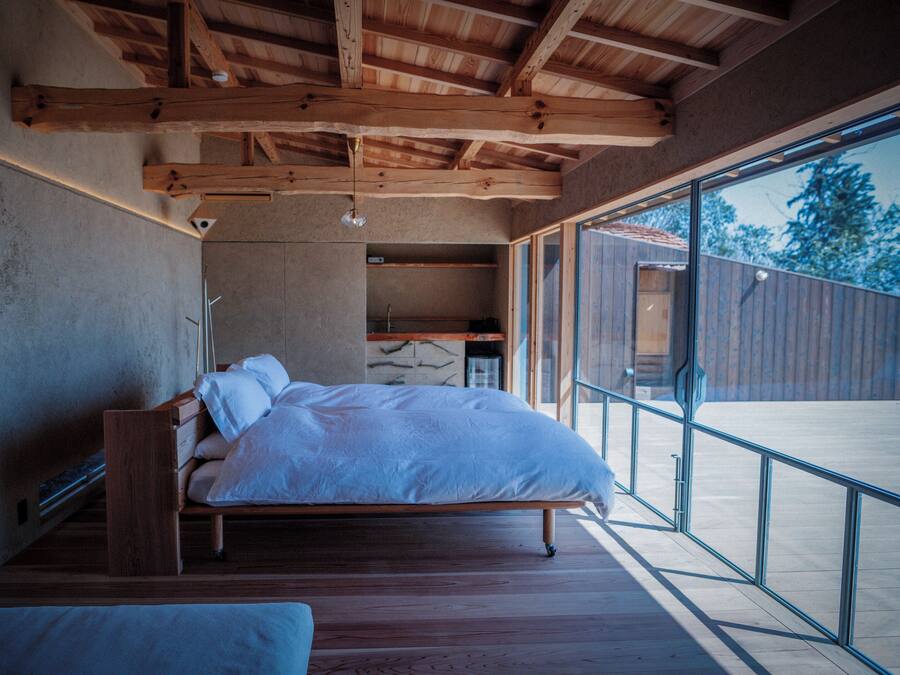 A bedroom with a wooden bed, a bench, and a large window.