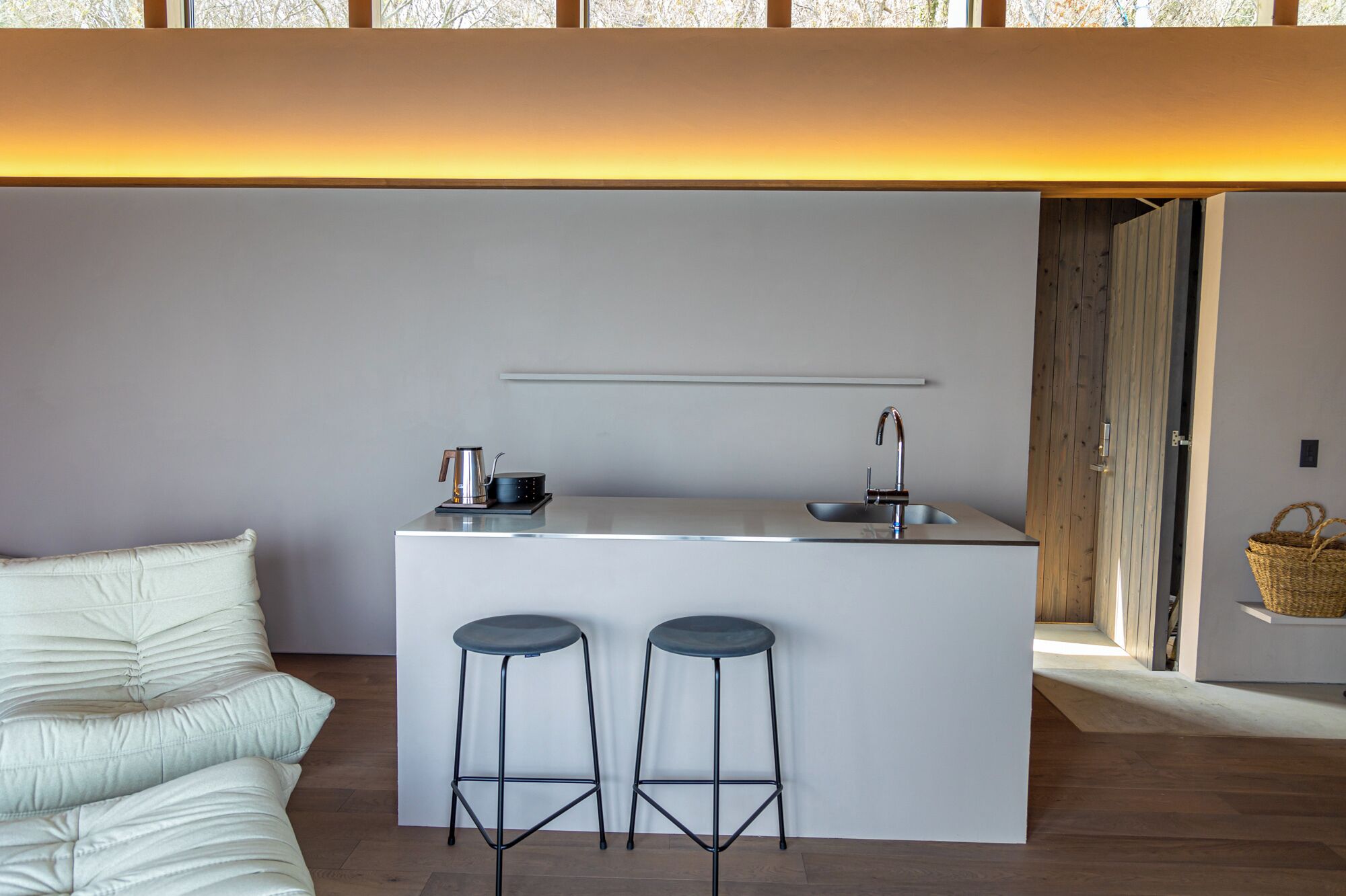 A modern kitchen with a white island, two stools, and a coffee maker.