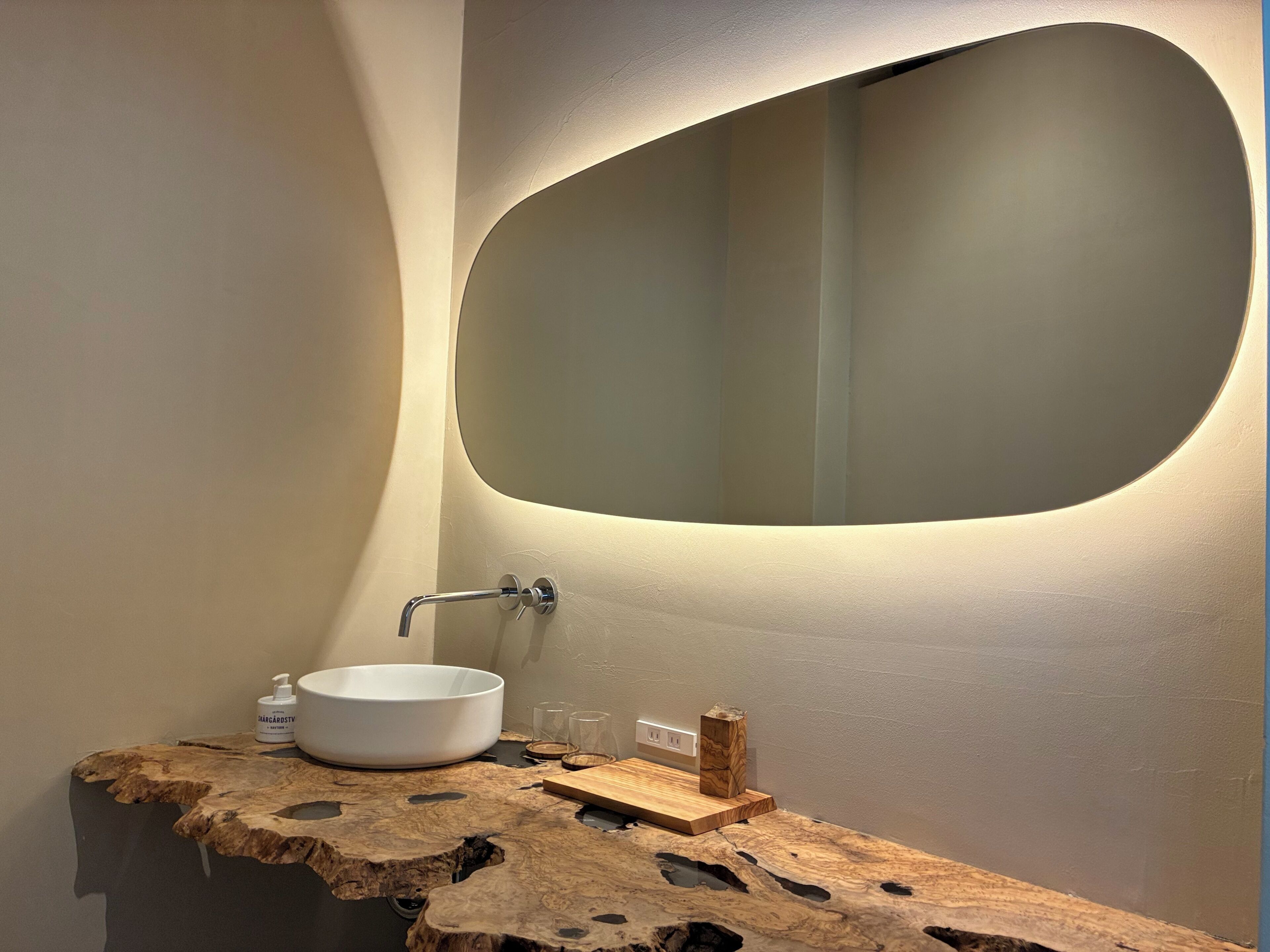 A bathroom with a round mirror, a white sink, and a wooden vanity.