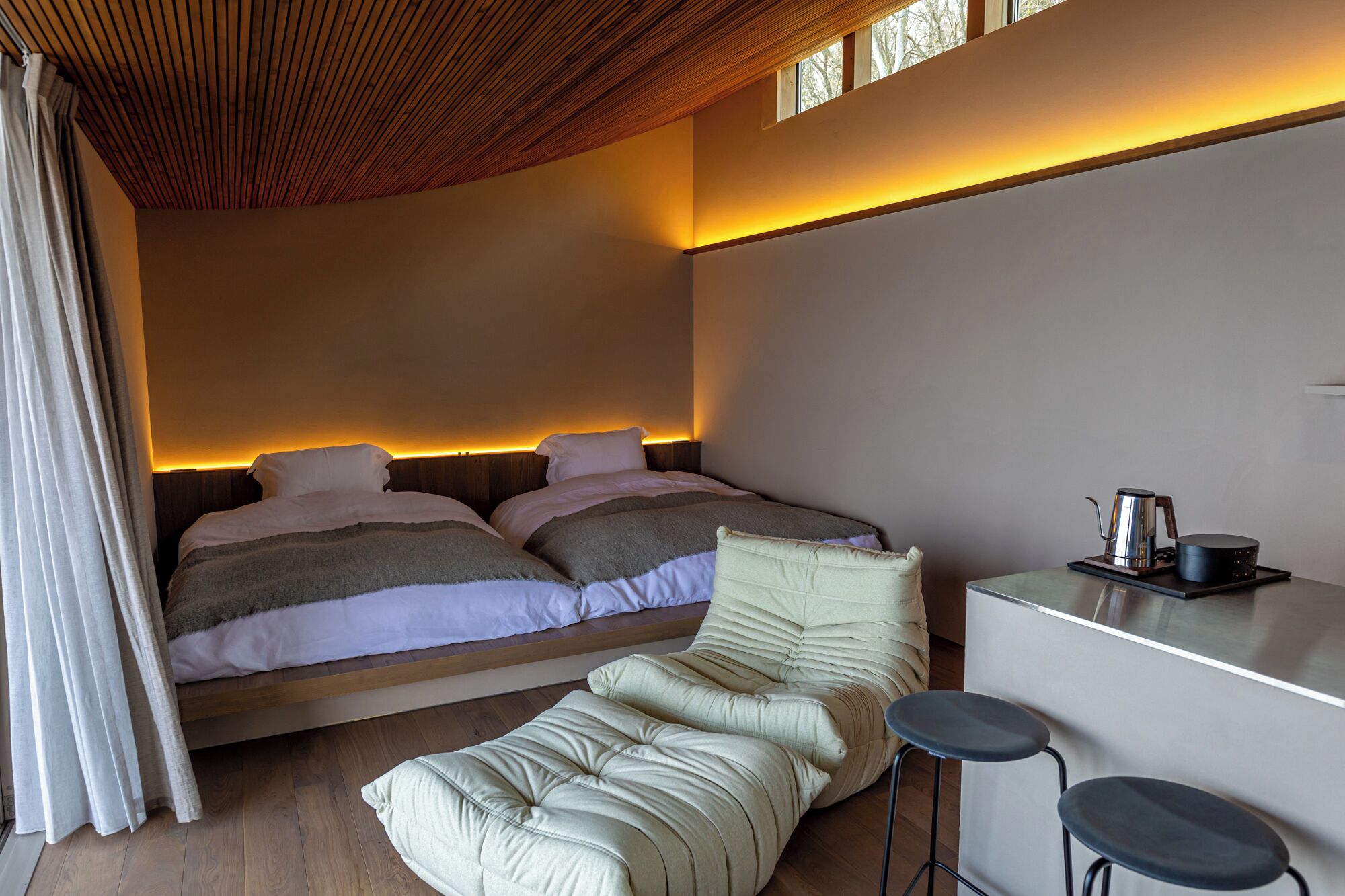 A modern bedroom with a bed, a sofa, and a small kitchenette.