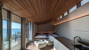 Un dormitorio moderno con un ventanal grande, techo de madera y lavamanos integrado.