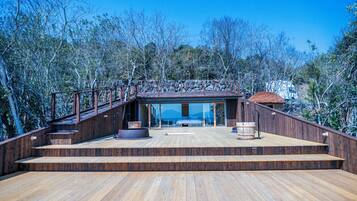 A wooden deck with a stone wall, a wooden staircase, and a glass door leading to a room.