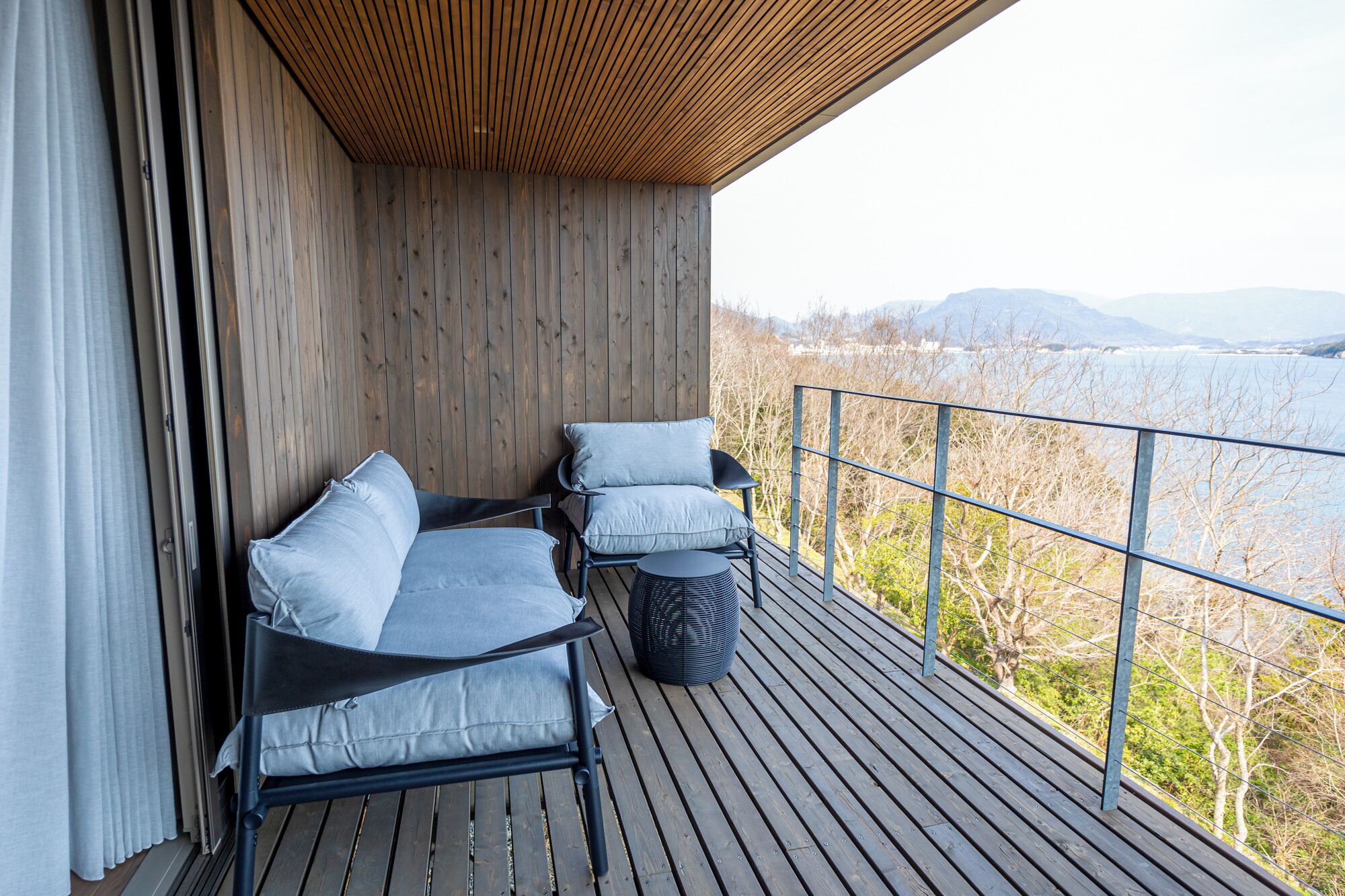 A balcony with two chairs and a round table, overlooking a scenic landscape with trees and mountains.