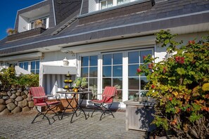Una casa con un patio attrezzato con tavolo e sedie, un muro in pietra e un'ampia finestra.
