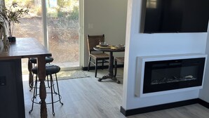Ein modernes Wohnzimmer mit Kamin, einem Essbereich mit Tisch und Stühlen sowie einem großen, an der Wand befestigten Fernseher.