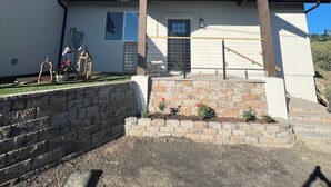 Ein modernes Haus mit Steinfundament, einer Garagentür und einem kleinen Garten mit Blumentöpfen.