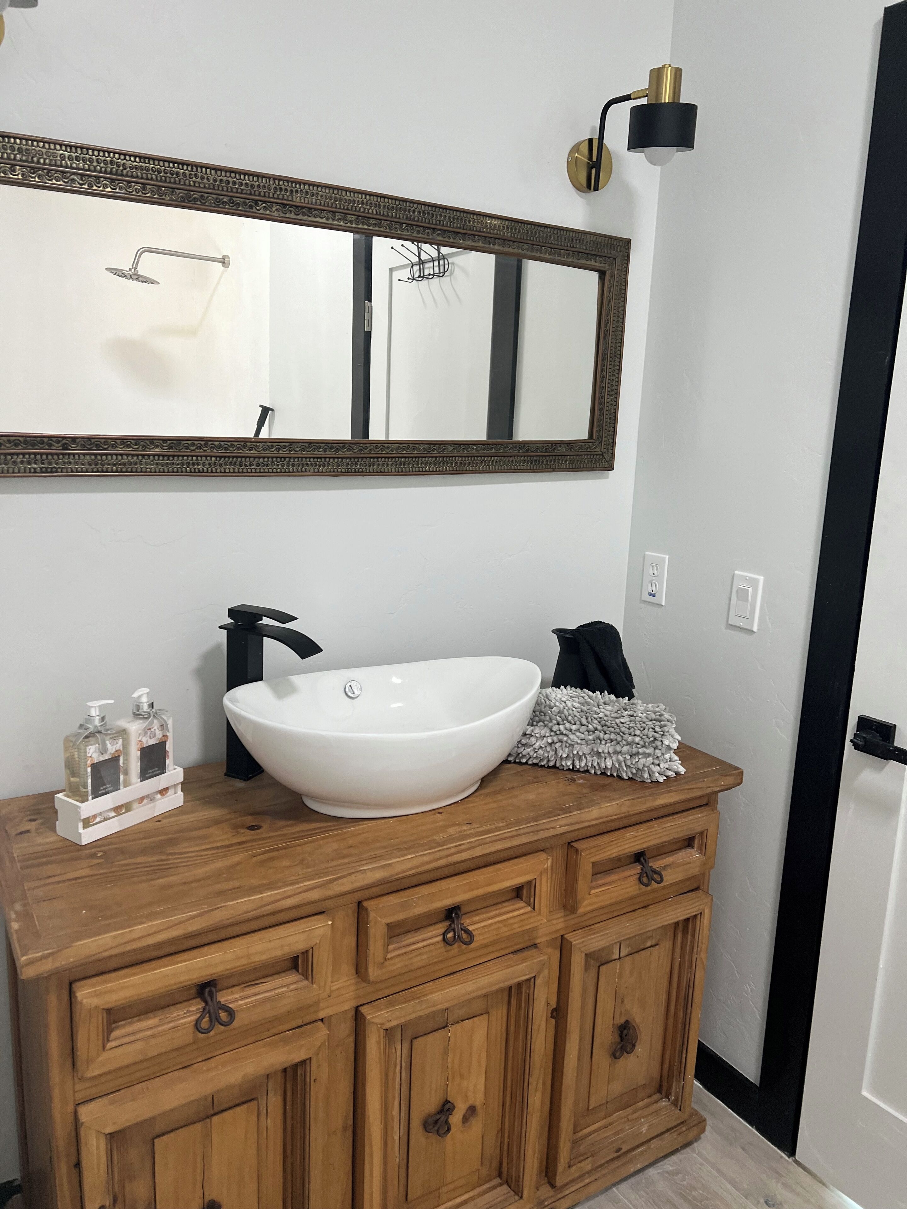 A bathroom with a white sink, wooden vanity, and a large mirror.