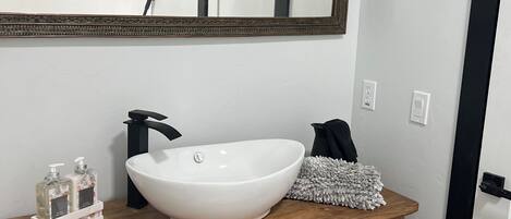 A bathroom with a white sink, wooden vanity, and a large mirror.
