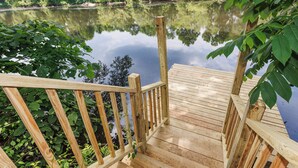 Una terraza de madera que conduce a un lago tranquilo rodeado de abundante vegetación.