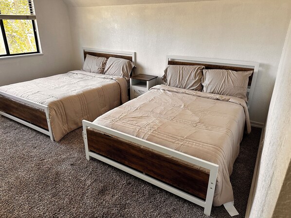 A bedroom with two single beds, a nightstand, and a window with blinds.