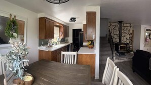 A modern kitchen with wooden cabinets, a dining area with a wooden table, and a living room with a fireplace. - THE SPOT, EAST SHORE (Westwood)
