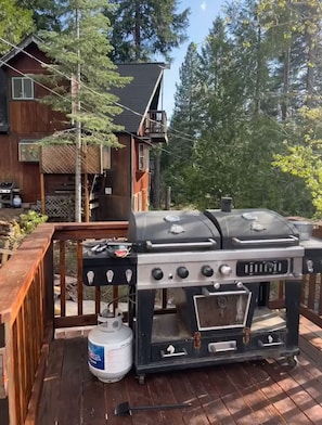 A barbecue grill with a gas tank on a wooden deck.