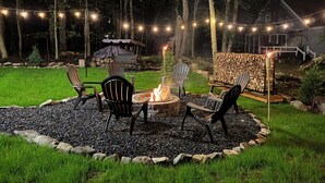 An outdoor seating area with a fire pit, surrounded by chairs, and string lights. - Fully new 3BR House in heart of Pocono Mountains, Fire Pit! Close to Water Park! (Tobyhanna)
