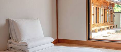 A neatly made bed with white linens in a room with wooden flooring and a large window.