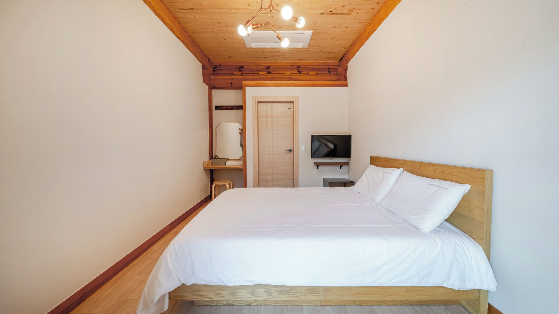 A bedroom with a wooden ceiling, a bed with white bedding, a television on a stand, and a door.